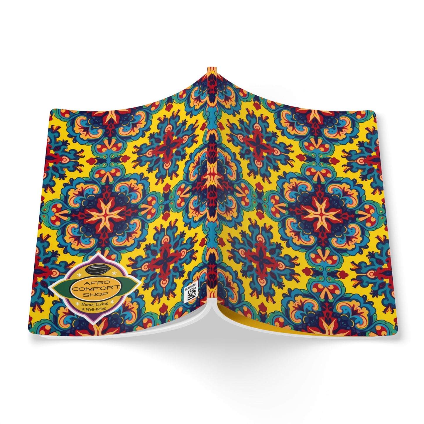 An open African-inspired journal features a vibrant, symmetrical floral pattern in blue, red, black, and orange on a yellow background. A gold hexagonal label on the back cover reads AFRO COMFORT SHOP with contact details below. Viewed from above.