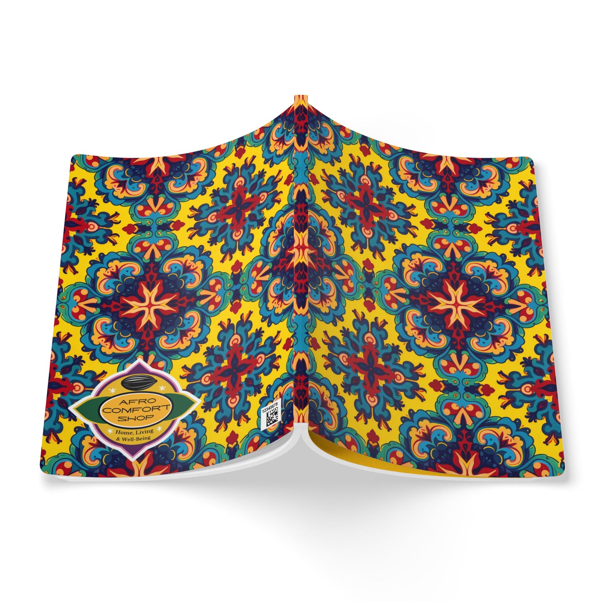 An open African-inspired journal features a vibrant, symmetrical floral pattern in blue, red, black, and orange on a yellow background. A gold hexagonal label on the back cover reads AFRO COMFORT SHOP with contact details below. Viewed from above.