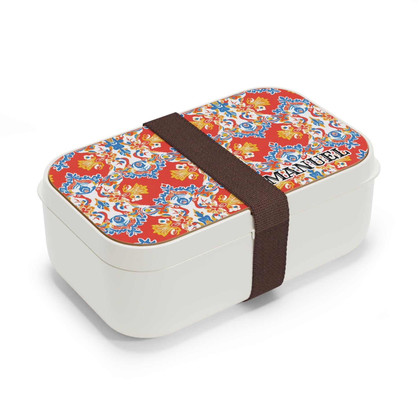 A rectangular white African-inspired bento lunch box is secured with a dark brown elastic band. The lid features a bright red background with a colorful, intricate floral pattern and the word MENU printed in black uppercase letters in the corner.
