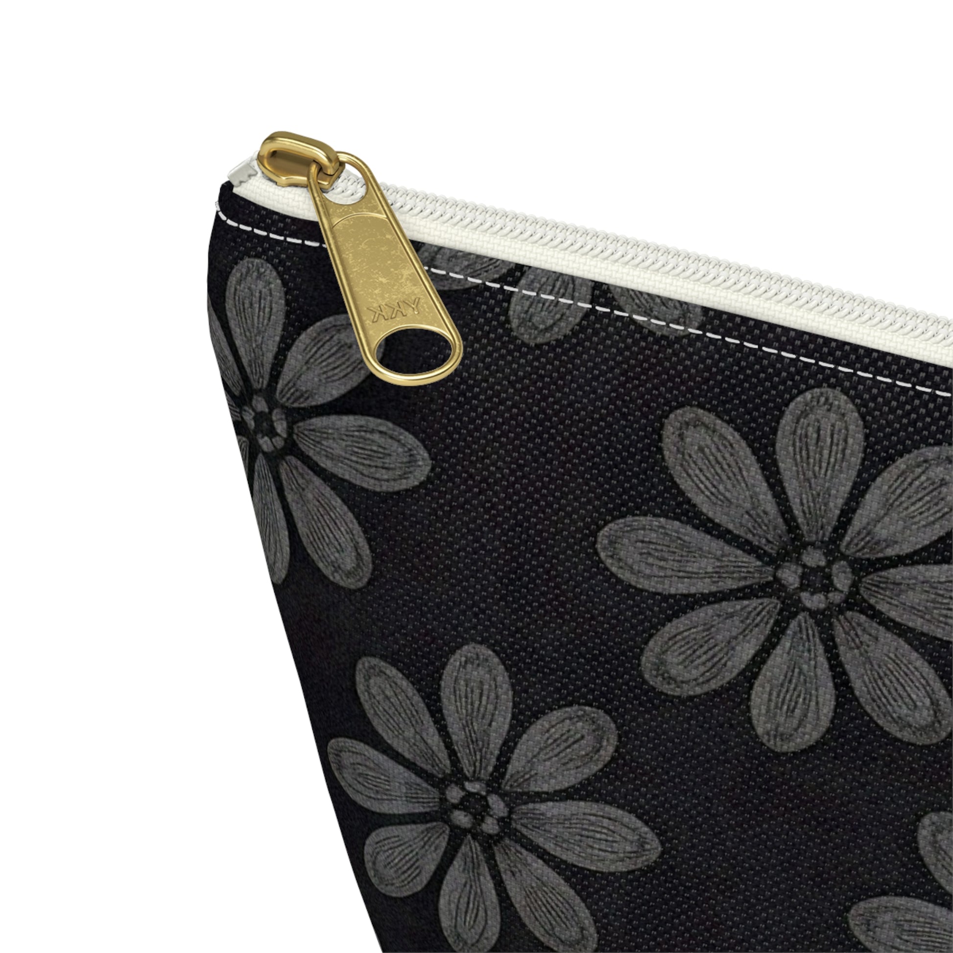 Close-up of a T-bottom pouch corner, featuring a white zipper with a gold pull tab. The fabric is black with large gray flowers in African-inspired patterns. Each flower has six textured petals and a central dot, with visible stitching along the top.