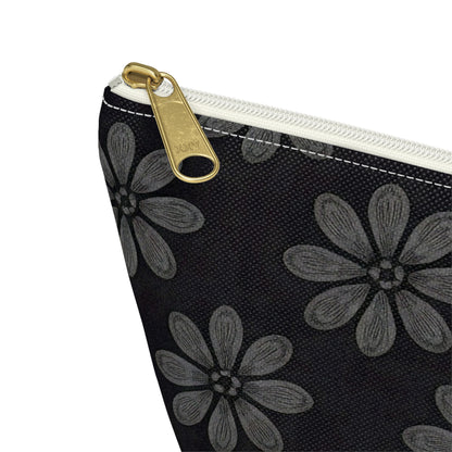 Close-up of a T-bottom pouch corner, featuring a white zipper with a gold pull tab. The fabric is black with large gray flowers in African-inspired patterns. Each flower has six textured petals and a central dot, with visible stitching along the top.
