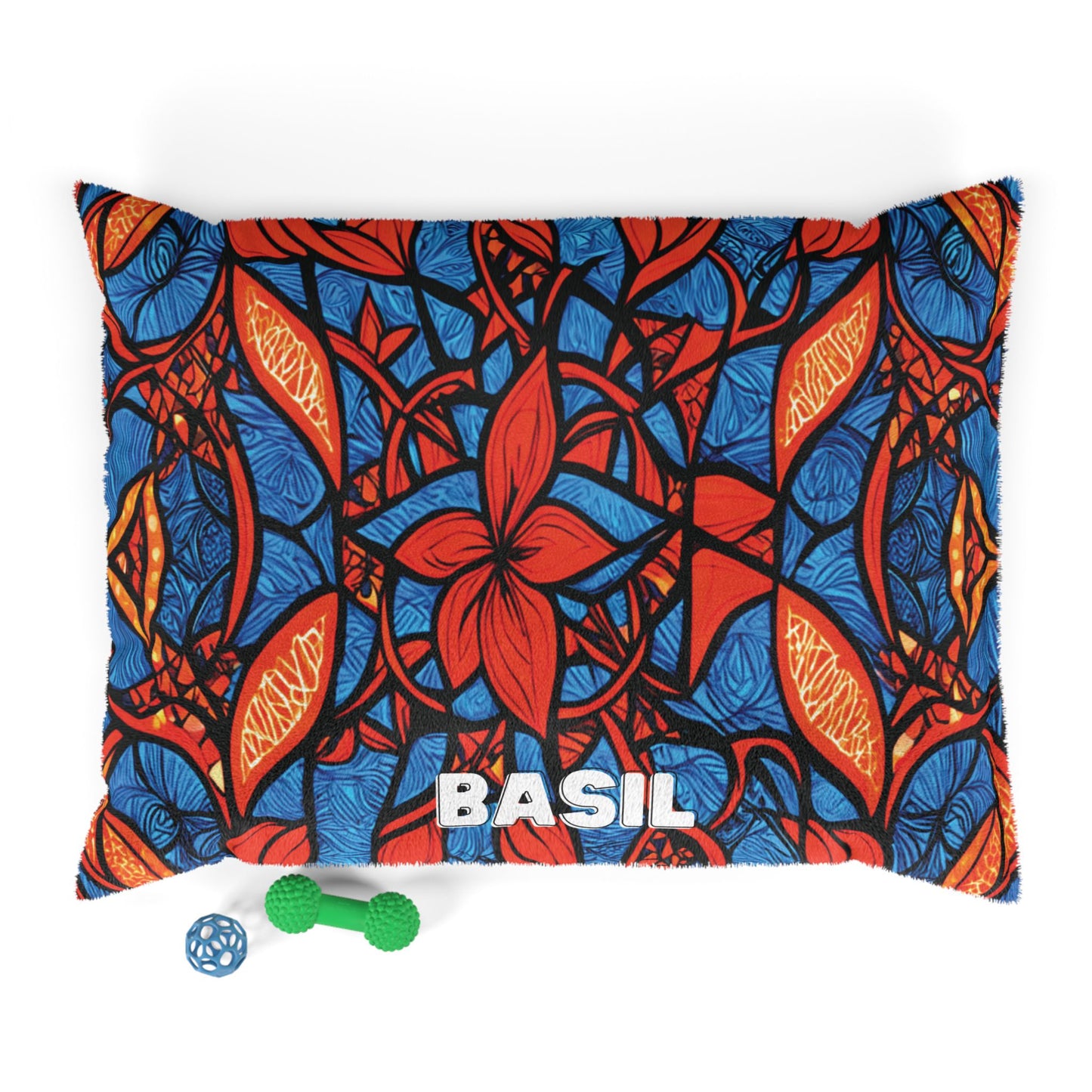 A stylish pet bed with BASIL printed on it features a bold, colorful pattern with large red flowers, orange leaves, and blue backgrounds. Two dog toys—a green bone-shaped toy and a blue ball—rest on the white floor below.