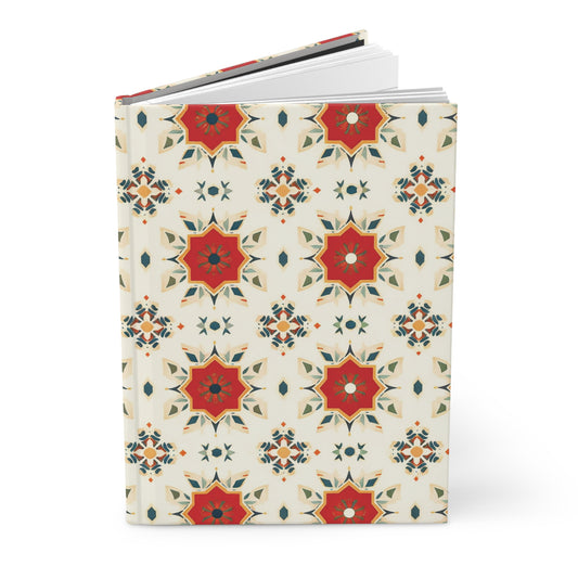 A hardcover wellness journal with a cream background features a repeating pattern of red, orange, and olive green geometric starburst motifs, creating a symmetrical and vibrant design reminiscent of an African-inspired journal. White pages are visible inside.
