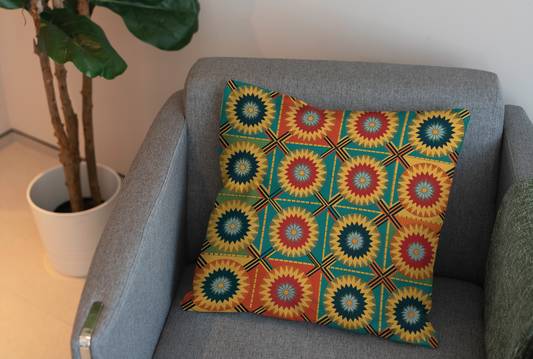 A square pillow with vibrant patterns and a colorful geometric starburst design in yellow, red, green, and blue rests on a light gray armchair. A green plant in a white pot sits nearby, adding charm to this inviting home decor scene.