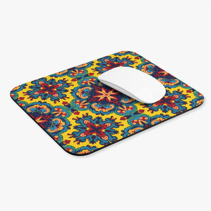 A white computer mouse rests on a rectangular African-inspired mouse pad with a vibrant, multicolored floral and geometric pattern on a bright yellow background. Featuring a non-slip rubber base, this vibrant desk accessory adds flair to any white workspace.