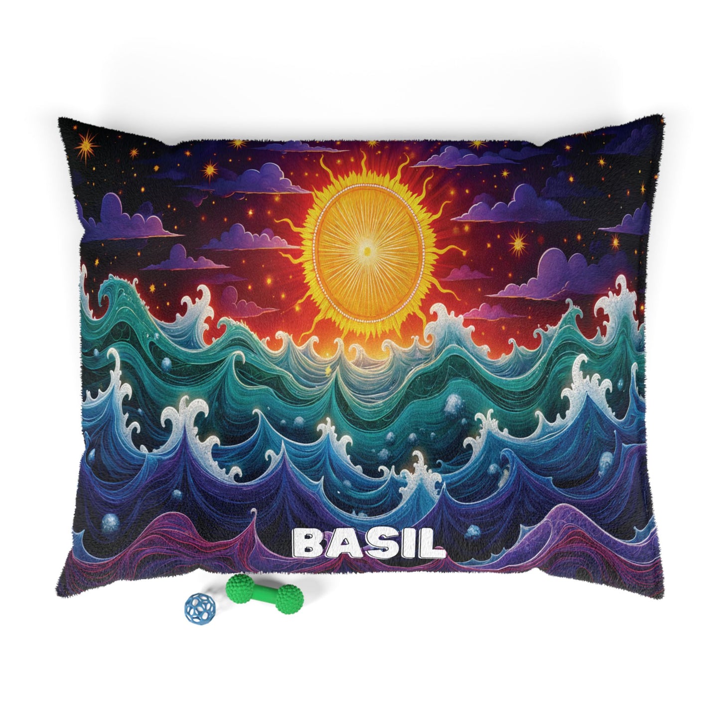 A rectangular personalized pet bed with the name BASIL at the bottom shows a colorful, stylized ocean with swirling waves and a radiant yellow sun above, set against a starry, partly cloudy sky. Below are a green textured bone toy and a blue ball.