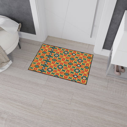 A rectangular doormat with a bright orange and yellow floral tile pattern adds African-inspired home decor flair on light wood flooring near a white door. A round white chair and a white shoe cabinet with beige shoes are visible nearby.