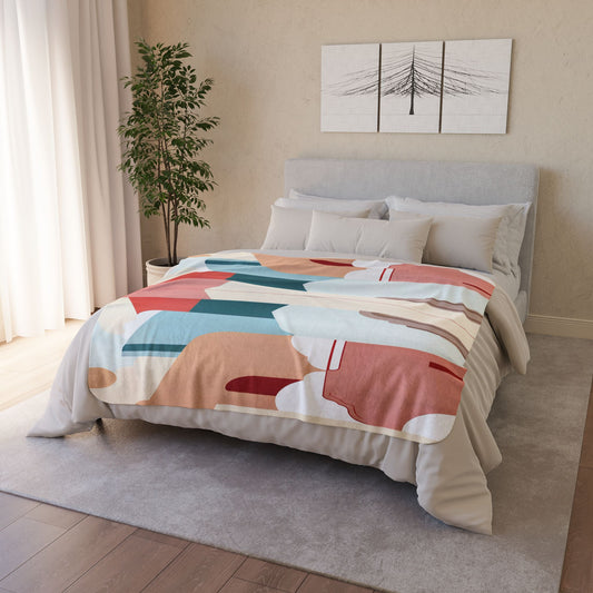 A neatly made bed with a colorful, African-inspired abstract-patterned comforter stands in a cozy bedroom. A plant is in the corner, sheer curtains cover a window, and two minimalist tree artwork panels hang above the light gray headboard.