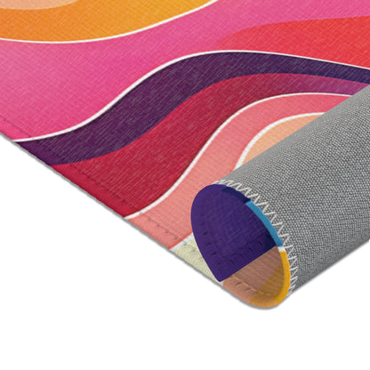 A close-up of an African-inspired rug corner featuring wavy lines in pink, orange, red, and purple hues. The rug is slightly rolled, revealing a gray textured underside with white zigzag stitching and a woven fabric surface.