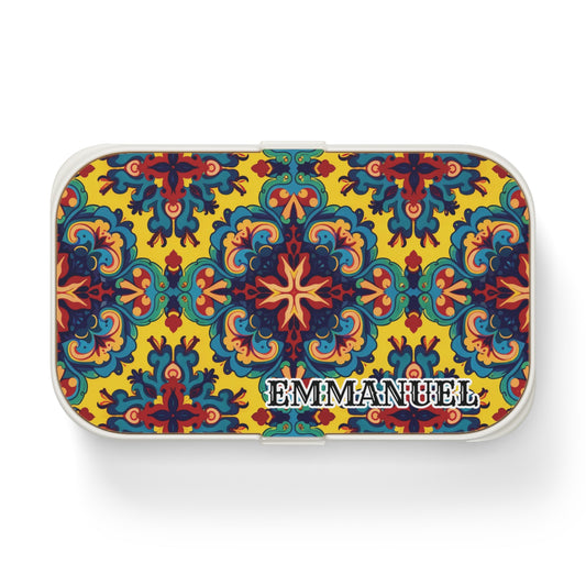 A rectangular, African-inspired bento lunch box with a vibrant, symmetrical floral and geometric pattern in red, blue, green, and yellow. The background is yellow, with EMMANUEL in bold white letters outlined in black at the bottom right corner.