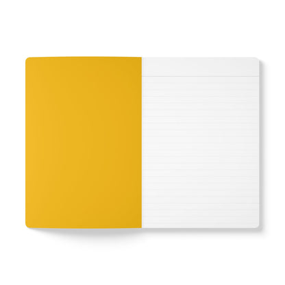 An open notebook on a white surface, ideal for creative journaling. The left page is solid mustard yellow, while the right page is white with light gray horizontal lines for writing. The notebook cover is not visible, and the lighting is bright and even.