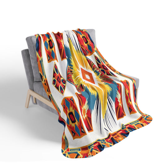 A gray, modern-style armchair is draped with an African-inspired vibrant blanket featuring a bold geometric pattern in red, orange, yellow, blue, and white, with a large central starburst and colorful shapes along the border. The background is plain white.