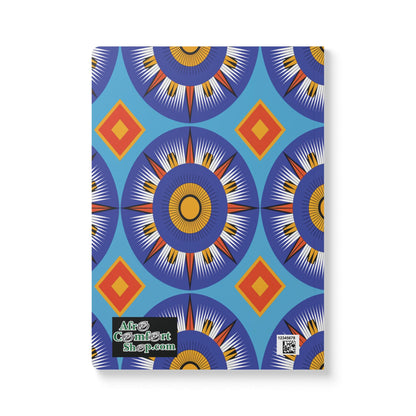 A notebook with a blue cover featuring a repeating geometric pattern of circular starbursts in orange, yellow, and navy, with red and orange diamonds between them. Perfect as an African-inspired journal for travel diary or creative journaling.