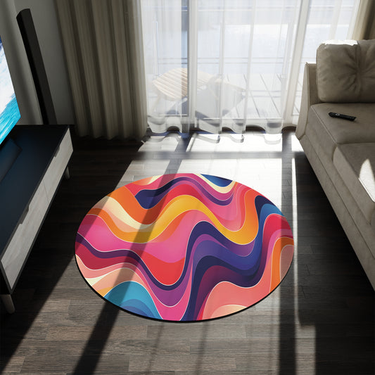 A bright, round, African-inspired rug with wavy, colorful patterns in pink, orange, yellow, red, blue, and purple sits on a dark wooden floor in a sunlit living room with a sofa, TV stand, sheer curtains, and glass doors.