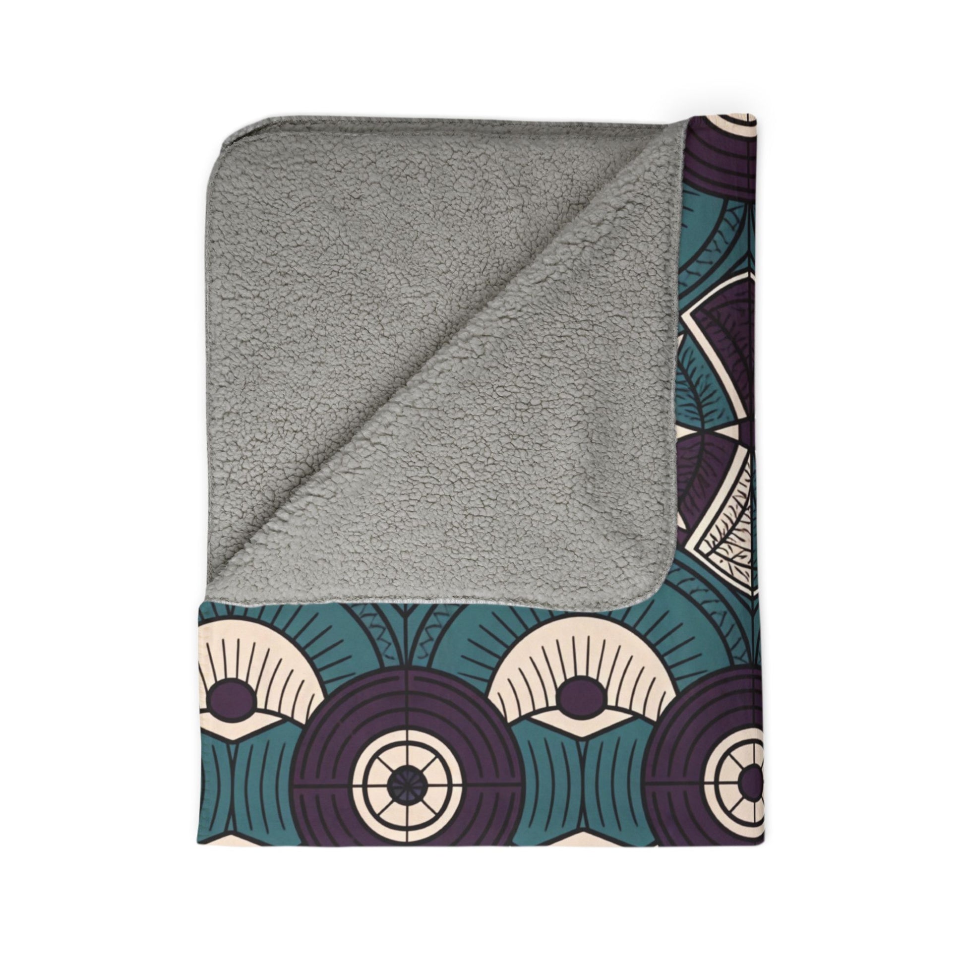 A sherpa fleece blanket with a gray, soft lining, partially folded to reveal an Art Deco pattern. This African-inspired fleece blanket features repeating arches in teal, purple, cream, and dark blue—perfect for cozying up your home decor.
