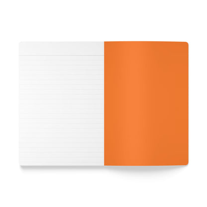 An open creative journal lies flat; the left page is lined and white, while the right side shows an orange cover folded back, hiding the opposite page. The white background emphasizes the notebook’s clean, minimal design.
