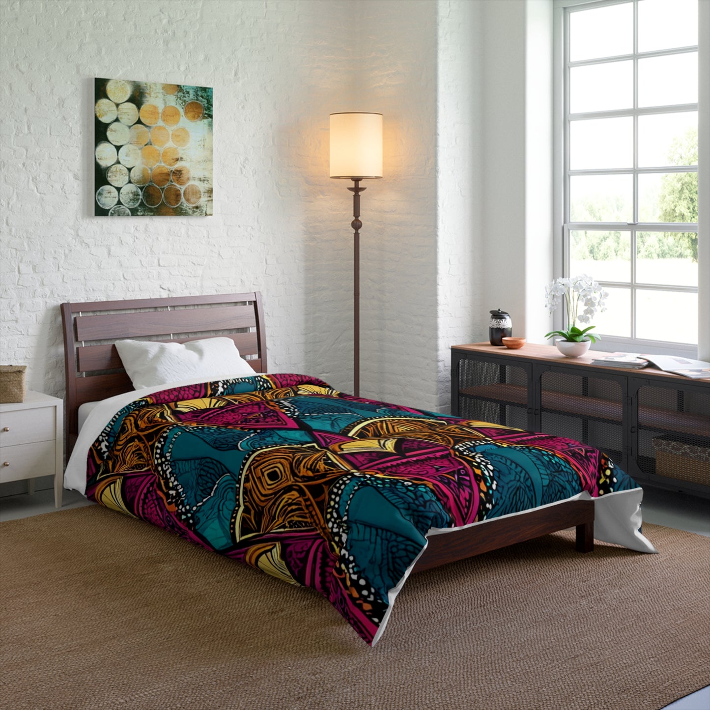 A modern bedroom with a low wooden bed, white bedding, and a colorful African-inspired geometric duvet in teal, pink, orange, and yellow. A tall floor lamp, art, wicker dresser, and sunlight from a large window complete the cozy space.