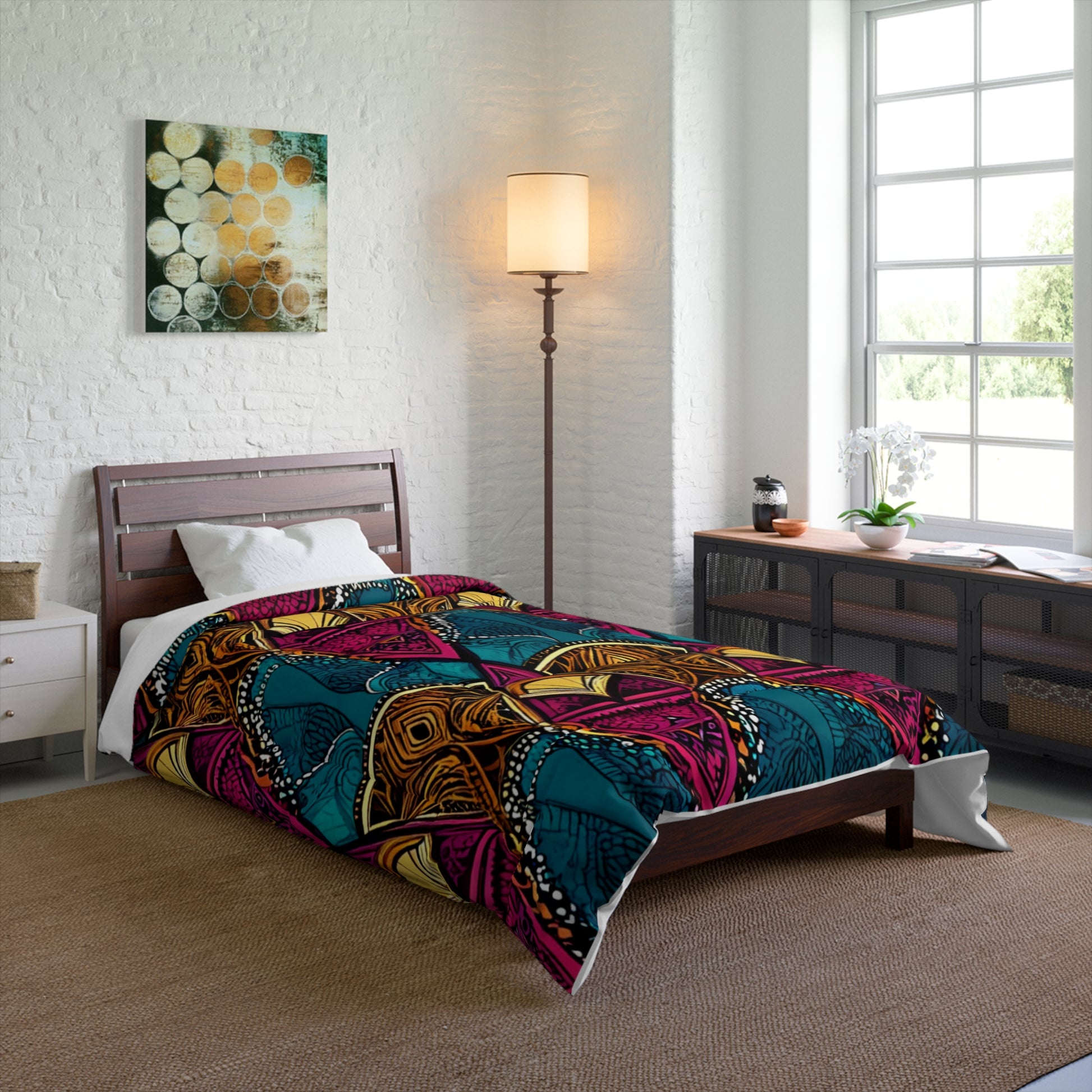 A modern bedroom with a low wooden bed, white bedding, and a colorful African-inspired geometric duvet in teal, pink, orange, and yellow. A tall floor lamp, art, wicker dresser, and sunlight from a large window complete the cozy space.