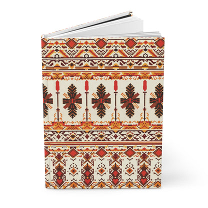 A hardcover journal featuring intricate, symmetrical folk-inspired patterns in red, orange, black, and yellow tones. The African-inspired design includes geometric shapes, crosses, stylized leaves, and repeating horizontal bands on a cream background.