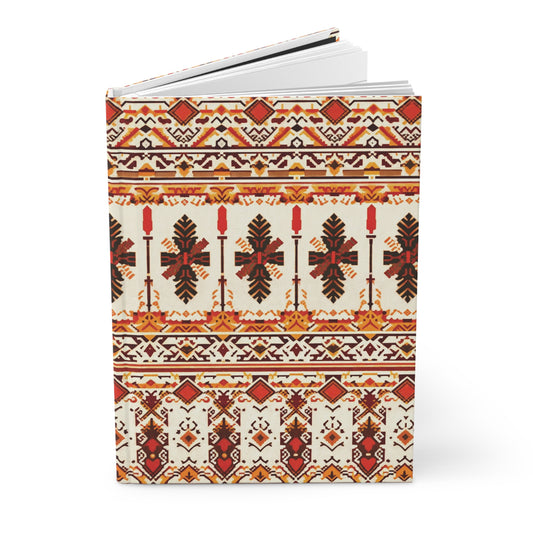 A hardcover journal featuring intricate, symmetrical folk-inspired patterns in red, orange, black, and yellow tones. The African-inspired design includes geometric shapes, crosses, stylized leaves, and repeating horizontal bands on a cream background.