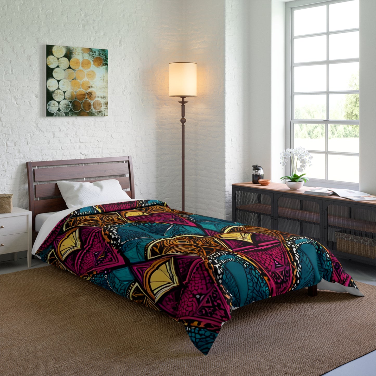 A modern bedroom with a single bed covered by a colorful African-inspired geometric-patterned comforter, a white pillow, tall floor lamp, large sunlit window, and a long console table with décor against a white brick wall.