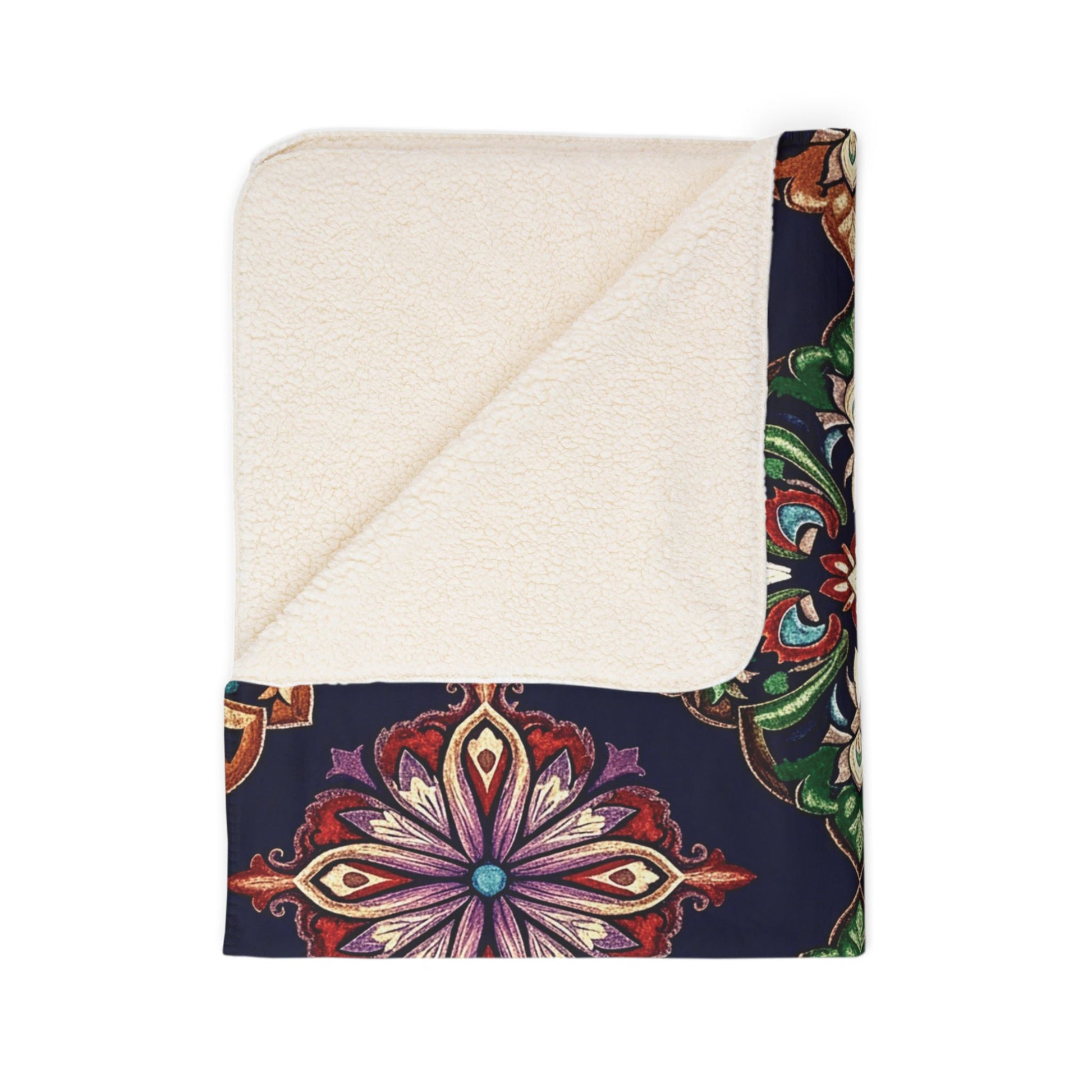 A folded sherpa-backed fleece blanket with a cream-colored, soft lining and dark exterior featuring a vibrant, symmetrical floral mandala in red, purple, green, and gold. One corner is turned down—perfect for cozy home decor.
