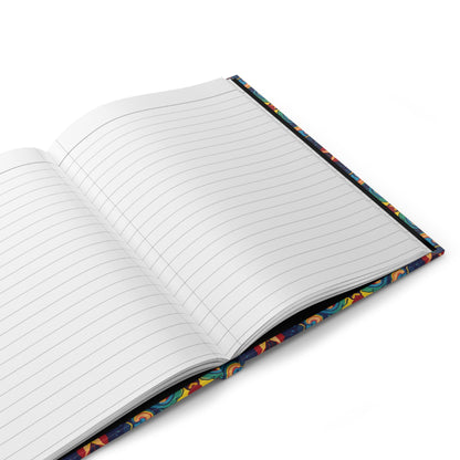 An open African-inspired journal with white, lined pages and a colorful, patterned cover featuring abstract designs. Resting on a white surface, the spine and part of the vibrant pattern are visible along the edges.