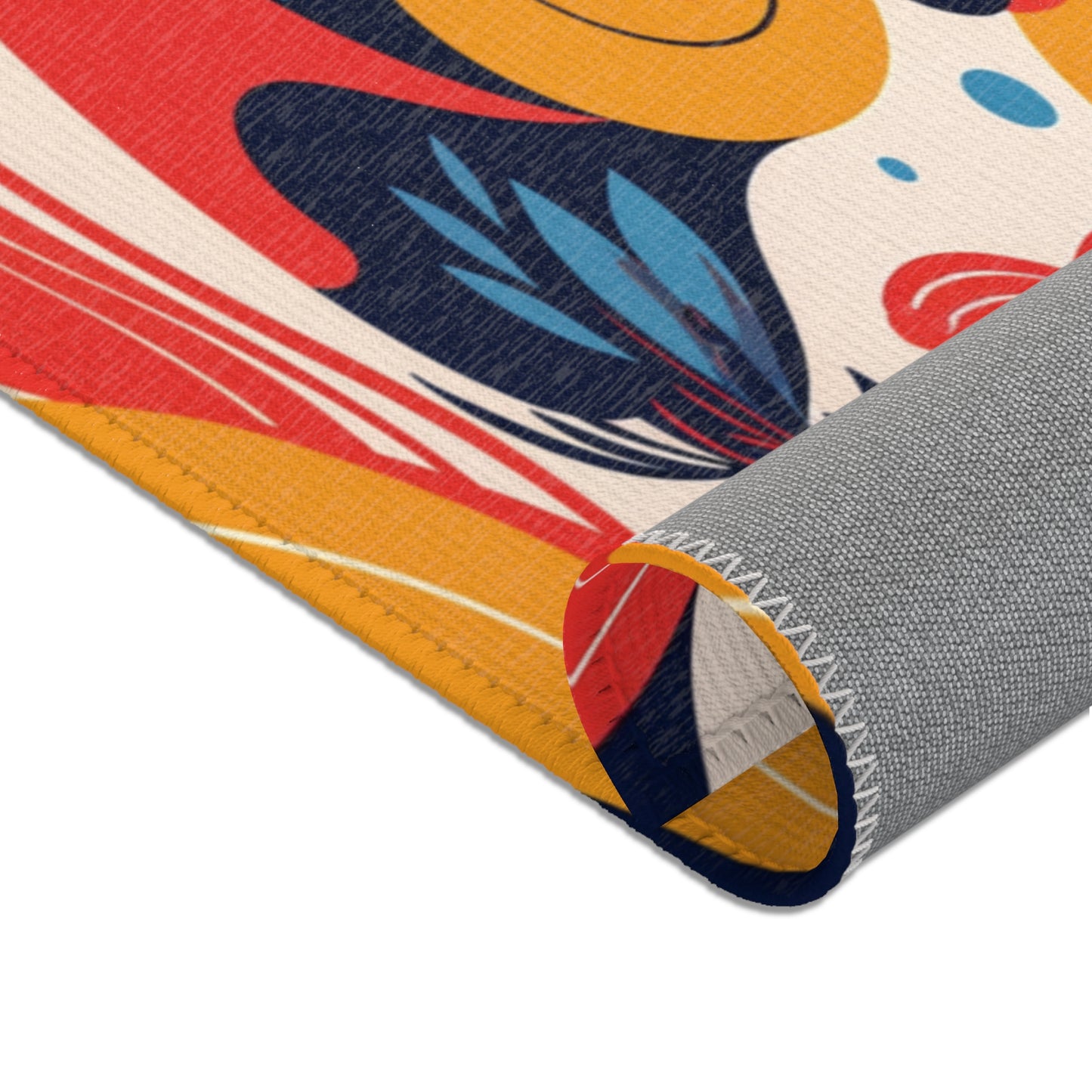 A close-up of a colorful fabric inspired by African design rugs, with bold abstract patterns in red, yellow, blue, white, and black. Clean stitching lines the edge and the durable polyester chenille is partially rolled to reveal a gray underside with a zigzag seam.