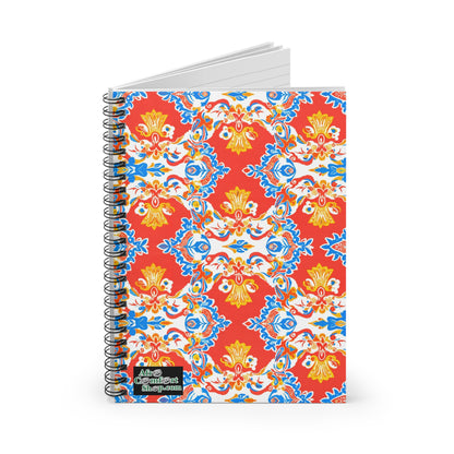A spiral-bound African-inspired spiral notebook with a vibrant red cover, intricate yellow, blue, and white floral patterns, and an “Aim Confident Shop.com” logo at the bottom left. The notebook is partially open to reveal premium writing paper.