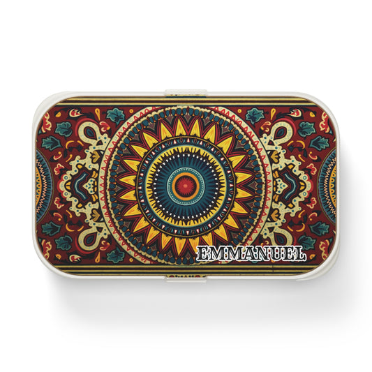 A rectangular tin box with a vibrant, symmetrical mandala pattern in red, yellow, blue, and green tones. This African-inspired lunch box features the name “EMMANUEL” in bold white letters on the bottom right corner of the lid.