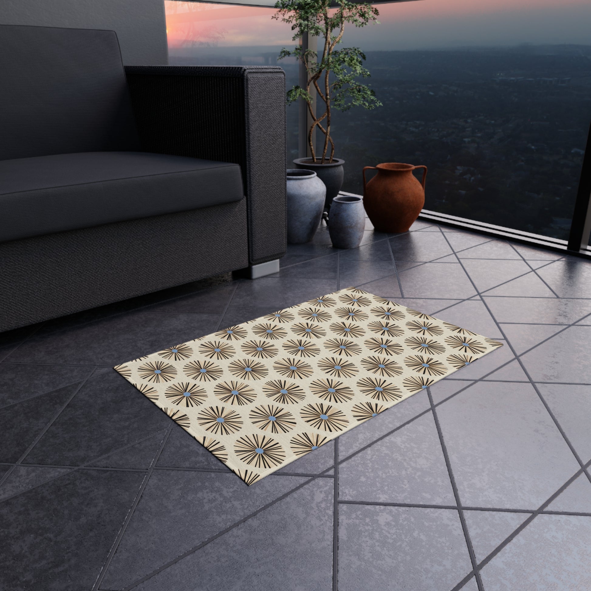 A beige weather-resistant polyester chenille rug with a repeating black starburst pattern lies on a tiled balcony floor. Nearby are a dark sofa and several decorative clay vases. In the background, there’s a glass railing overlooking a scenic cityscape at sunset.