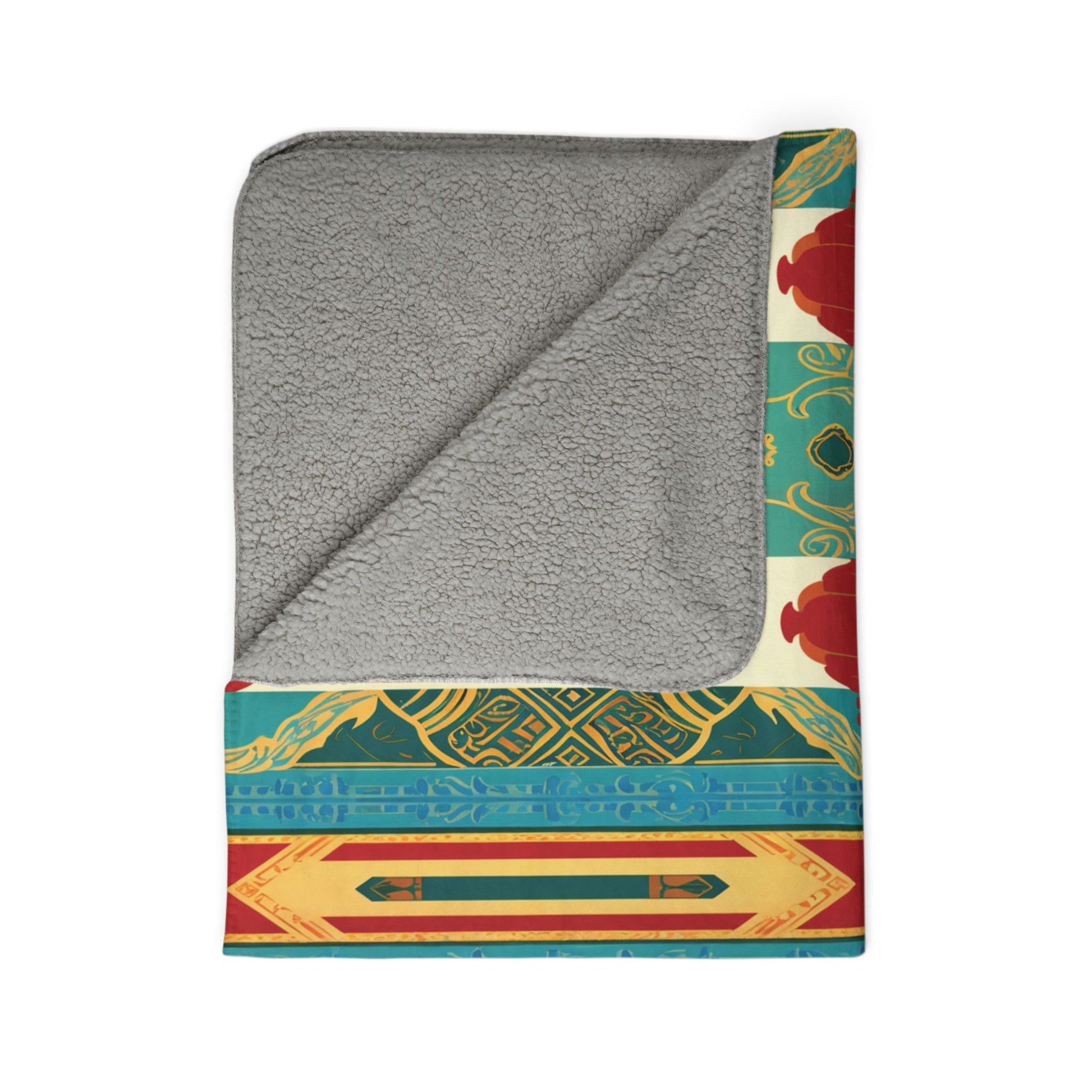 A folded blanket with a soft, gray, fleece-like interior and an African-inspired, colorful patterned exterior featuring teal, gold, red, and yellow geometric and ornamental designs. One corner is flipped to show the gray lining on a white background.