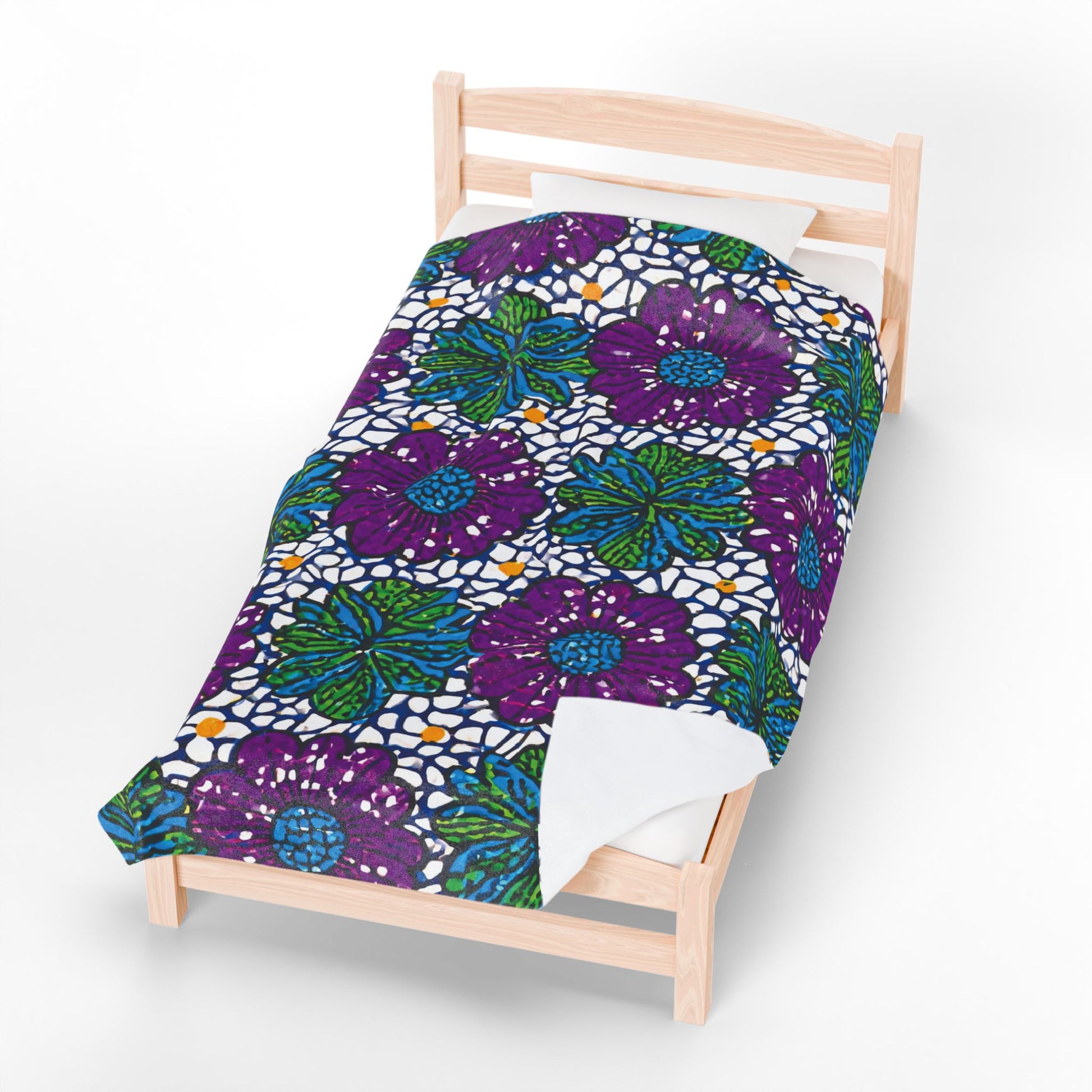 A light wooden bed with a white pillow and a vibrant African-inspired personalized blanket featuring bold purple and blue flowers, green leaves, and yellow accents on a white mosaic-like background. The blanket covers most of the bed.