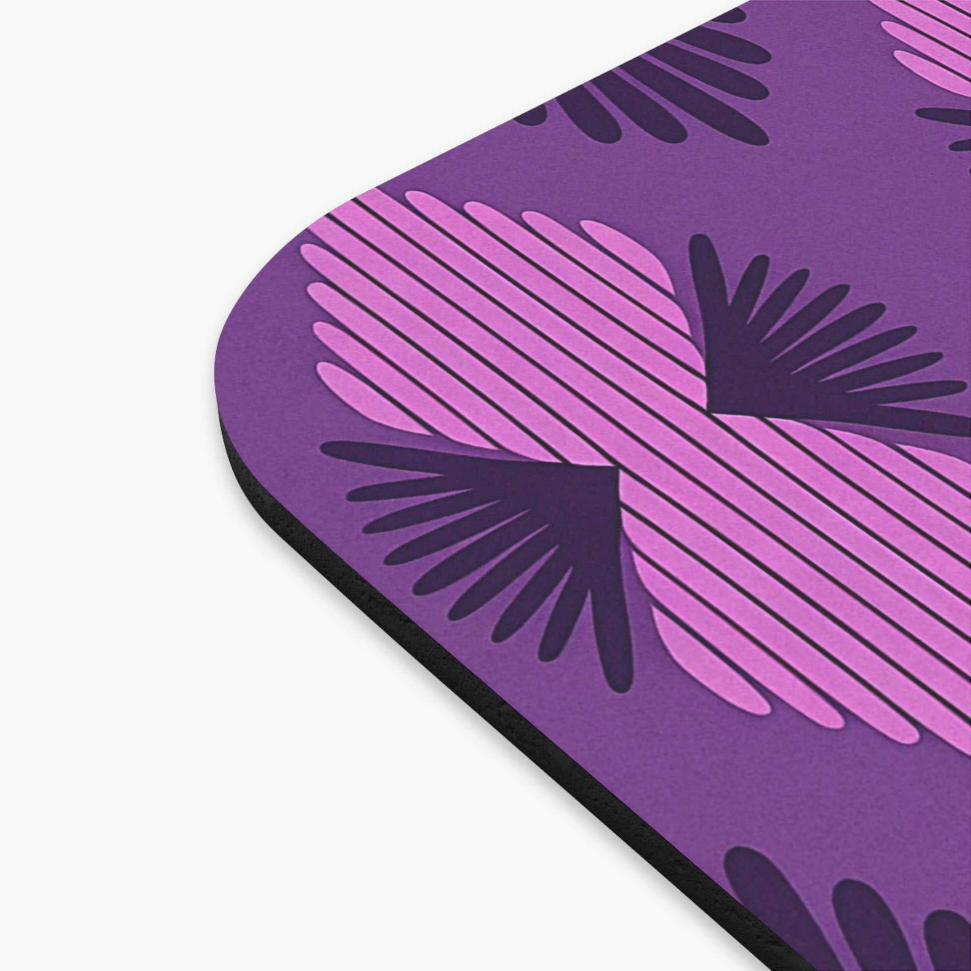 A close-up of an African-inspired mouse pad with a geometric pattern of dark purple and pink shapes resembling stylized wings. This durable desk accessory features rounded edges, a black side, and a non-slip rubber base for stability.