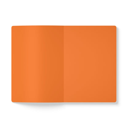 An open, blank creative journal with orange pages lies on a white surface. The notebook is viewed from above, showing the center crease and smooth, unmarked pages, perfect for daily journaling, with a subtle shadow on the left side.