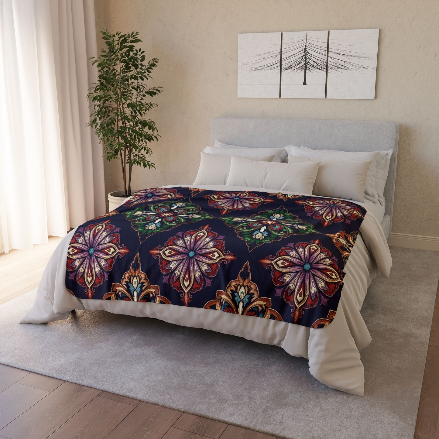A modern bedroom with a bed featuring an African-inspired fleece blanket in colorful, ornate floral patterns on dark fabric. The light gray headboard, neutral bedding, potted plant, and abstract art create a cozy home decor vibe.