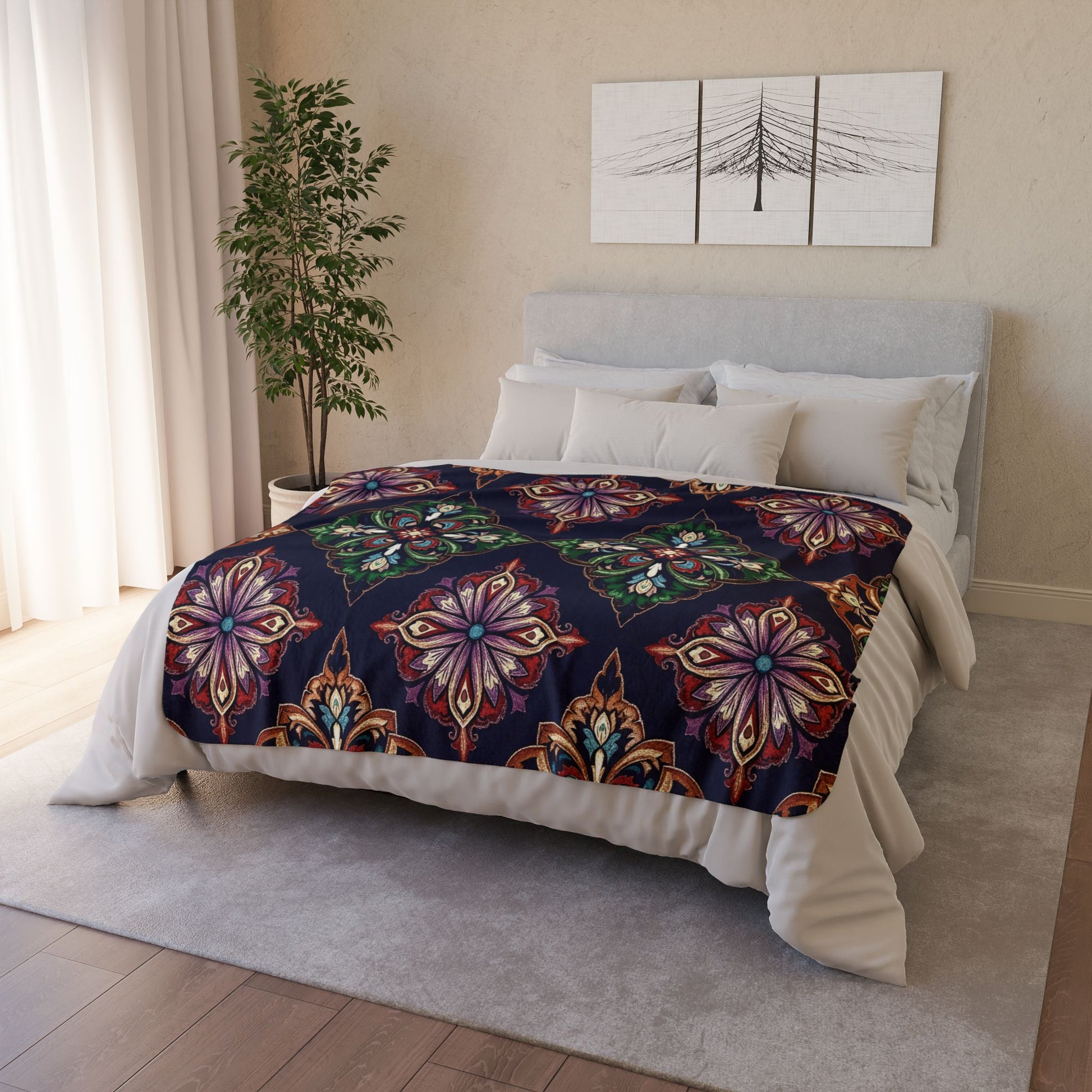 A modern bedroom with a bed featuring an African-inspired fleece blanket in colorful, ornate floral patterns on dark fabric. The light gray headboard, neutral bedding, potted plant, and abstract art create a cozy home decor vibe.