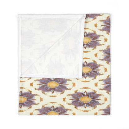 A folded fabric napkin featuring a symmetrical, African-inspired decor pattern with large purple-blue and yellow flowers on cream. One corner is folded to reveal the plain white underside, perfect for adding a vibrant touch to your table setting.
