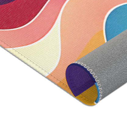 A close-up of a rolled-up, African-inspired mouse pad featuring colorful, wavy patterns in red, pink, cream, yellow, orange, and blue. The pad’s corner shows detailed reinforced edge stitching and a textured gray underside for grip.
