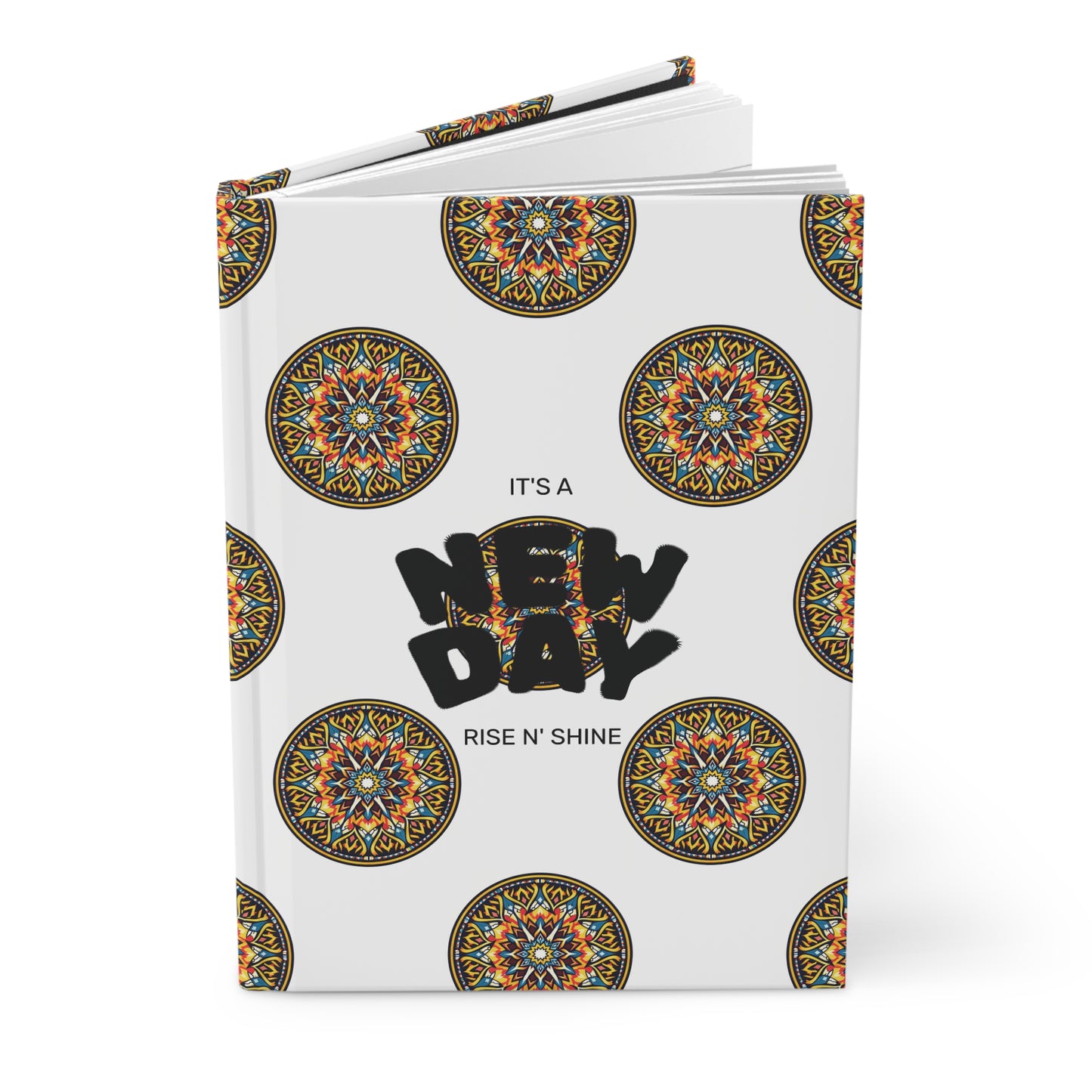 A hardcover journal with a white cover decorated with colorful circular mandala patterns. Centered bold black text reads “NEW DAY,” with smaller text above and below stating “IT’S A” and “RISE N’ SHINE.” Perfect for your wellness ritual, the notebook is slightly open.