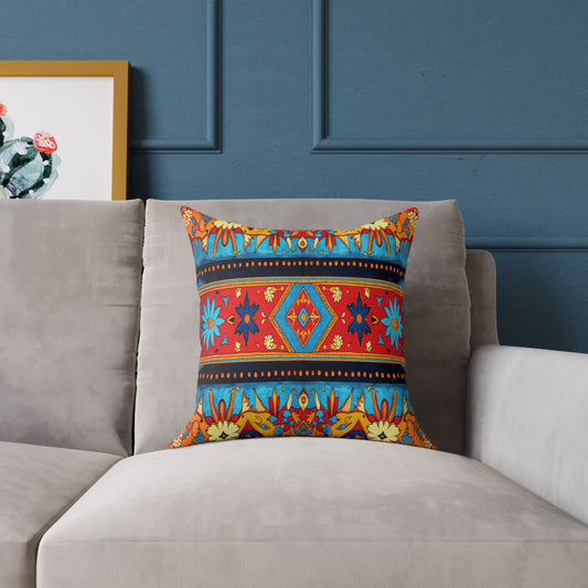 A colorful accent pillow with a bold geometric and floral pattern in red, blue, yellow, and orange sits on a light gray sofa against a dark blue wall, adding vibrant home decor beside a framed cactus artwork partially visible on the left.