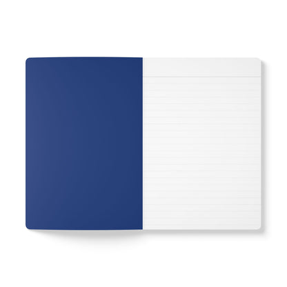 An open African-inspired journal is shown from above. The left page is solid dark blue, while the right is white with light gray horizontal lines for daily journaling. The background is plain white.