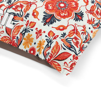 A close-up of a cushion corner with a vibrant African-inspired floral pattern in red, orange, and dark blue on a white background. The fabric appears textured, possibly faux fur, with part of a white embroidered letter visible on the left edge.