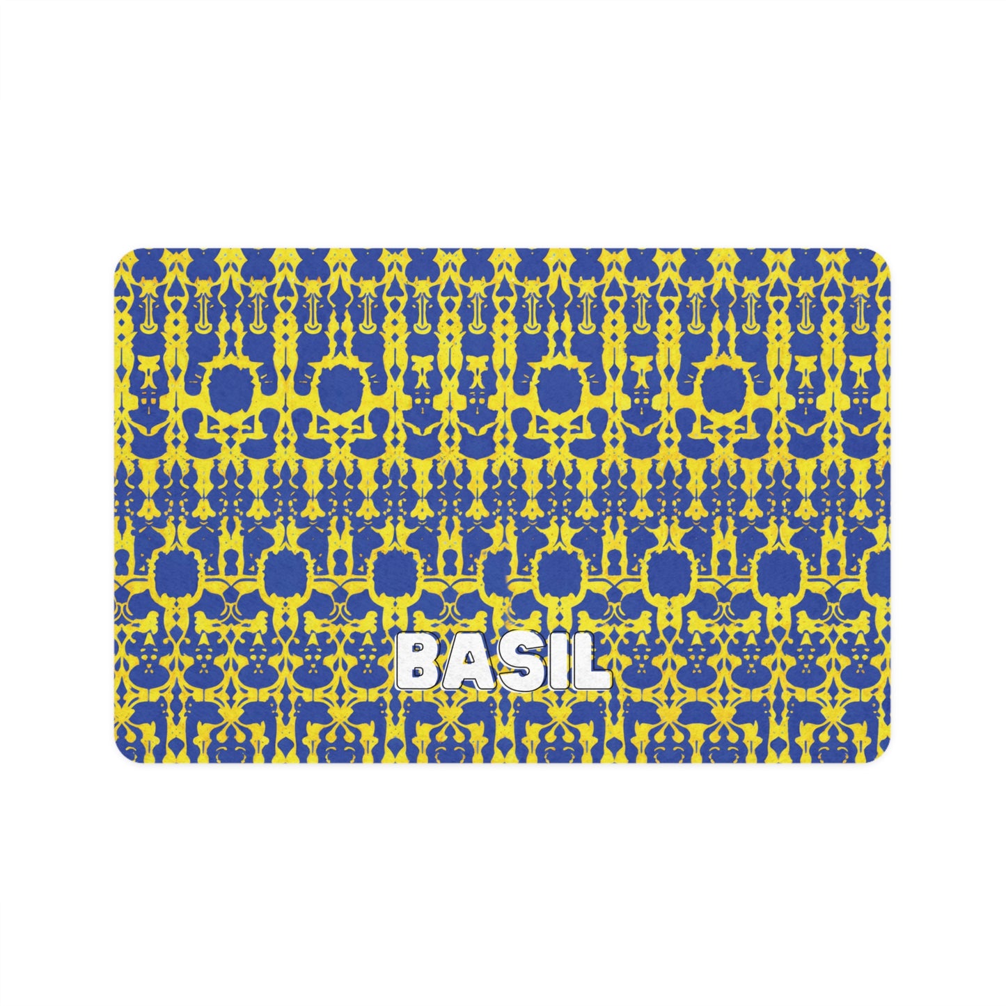 A rectangular mat with a bold blue and yellow symmetrical geometric pattern. The African-inspired, repeated shapes create an abstract, kaleidoscopic effect. The word BASIL in large, white, bold letters is centered near the bottom of the mat.
