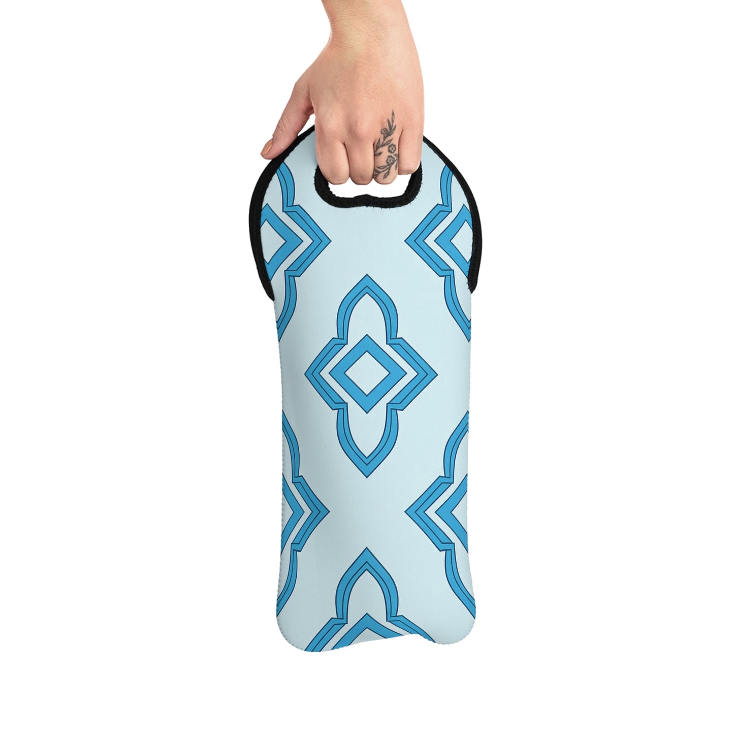 A hand with a floral tattoo holds a light blue insulated bottle carrier with a geometric blue pattern and black trim. Styled as an African design wine carrier, it features a curved handle at the top for easy carrying.