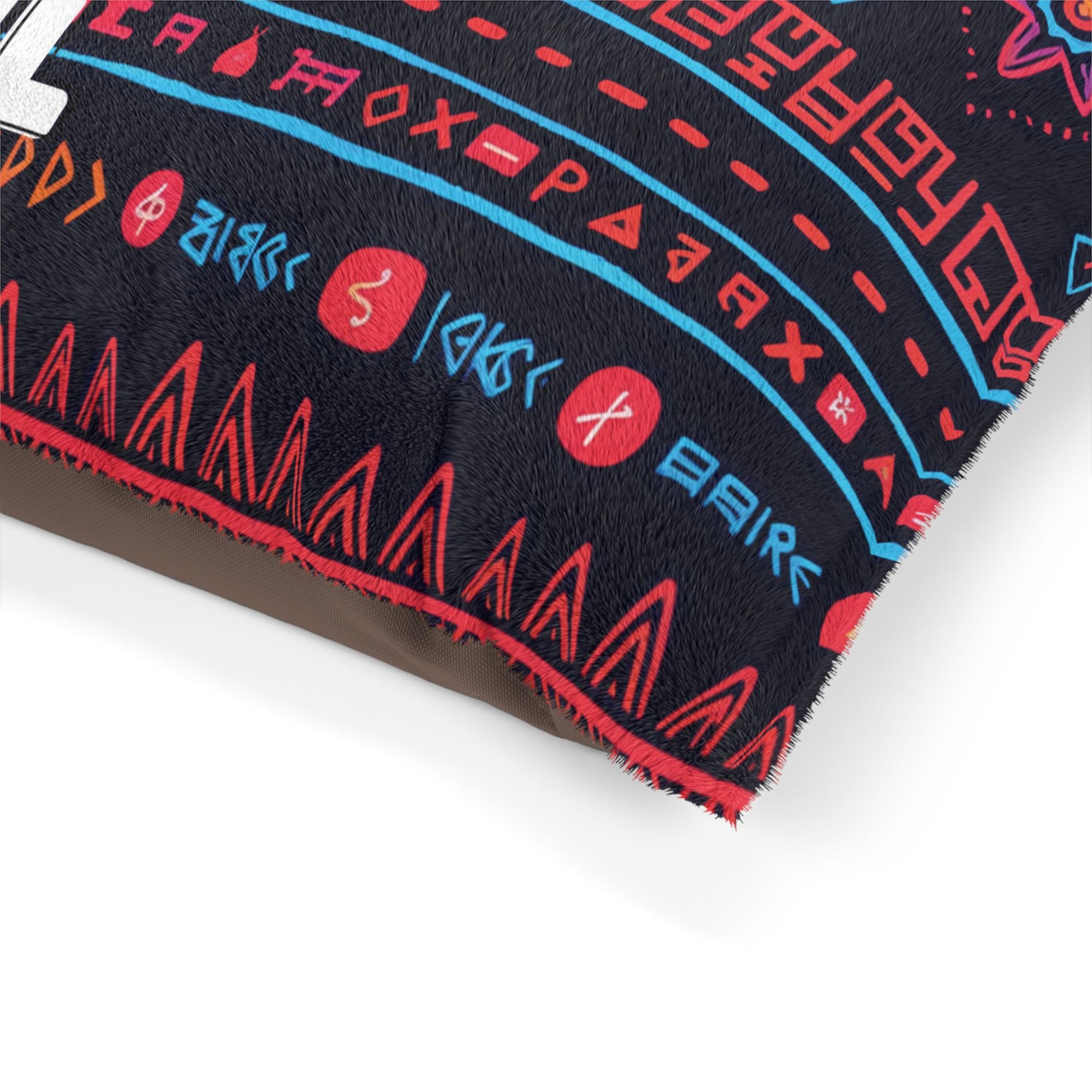 A close-up of an African-inspired pillow with a black fabric cover featuring vibrant red and blue geometric designs, patterns, and runic symbols. The pillow’s edge is trimmed with red zigzag stitching, and the surface has a faux fur texture.