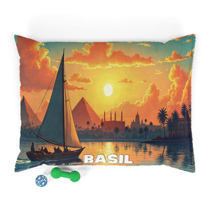 A rectangular pillow with durable construction features a vivid sailboat scene at sunset, pyramids, palm trees, and a mosque silhouette. “BASIL” is printed at the bottom. Two dog toys rest nearby, perfect for personalized pet beds.
