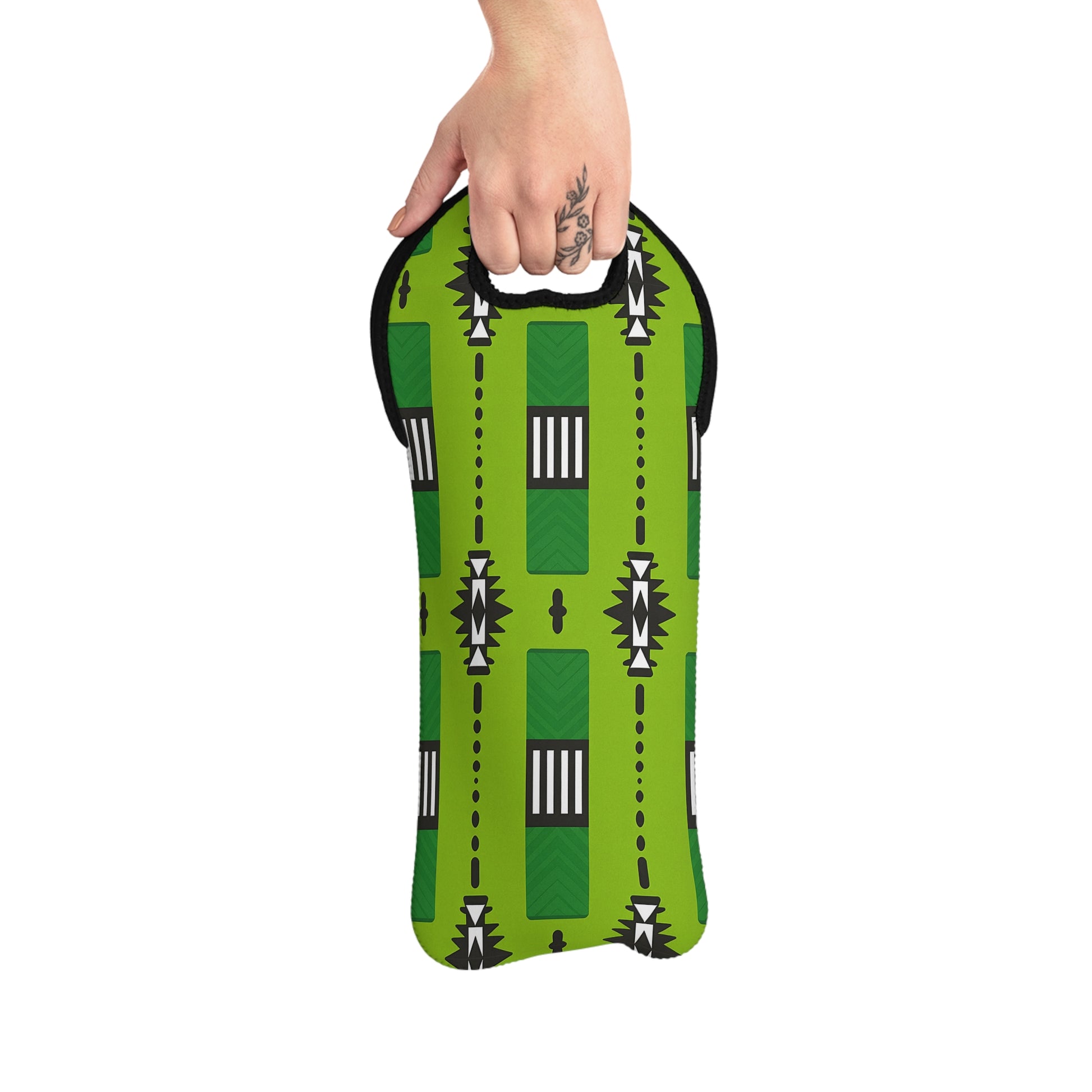 A hand with a floral tattoo holds an insulated wine bag, featuring a bold geometric pattern inspired by African design. This green neoprene wine tote has black trim and a cut-out handle at the top for easy carrying.