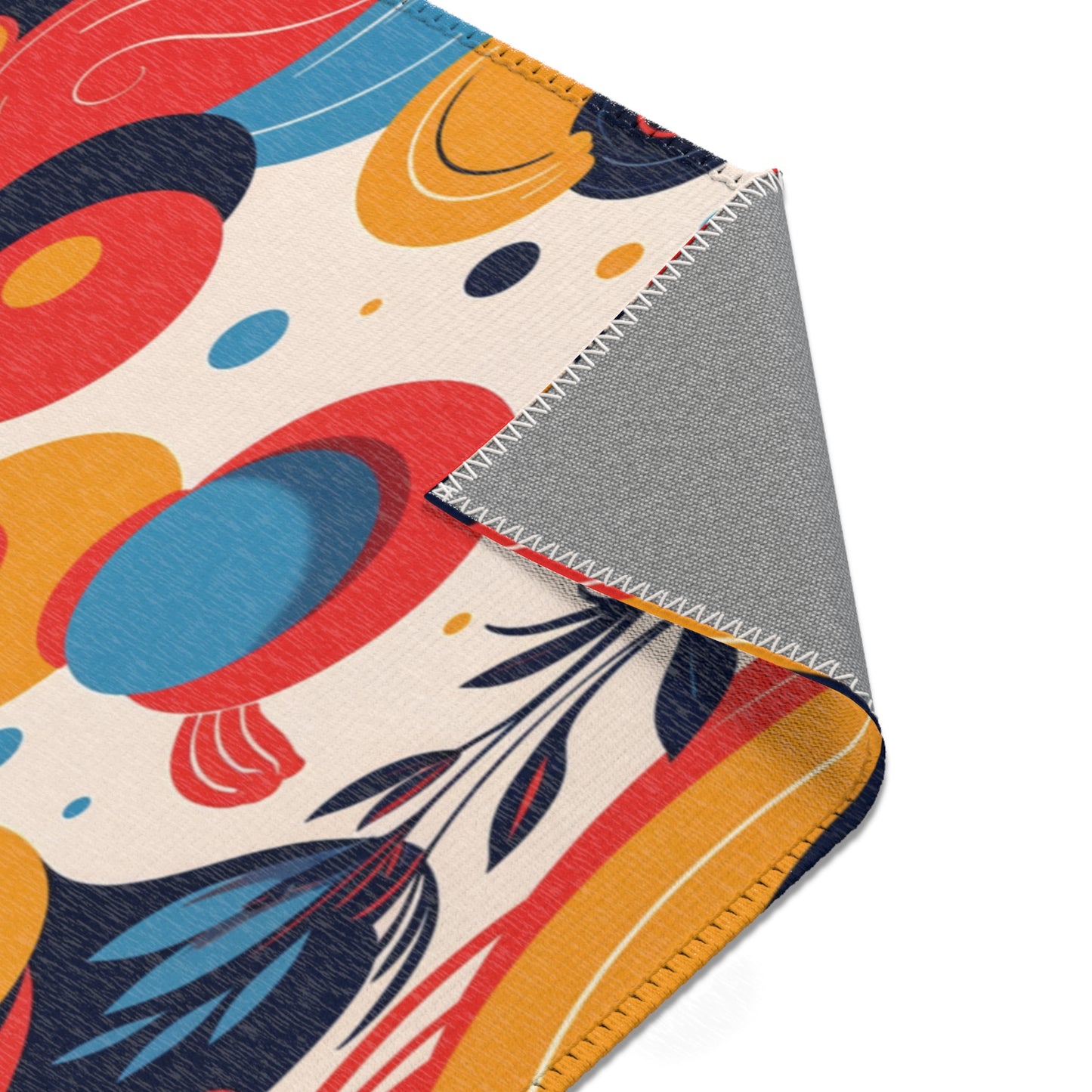 A close-up of a blanket with a colorful abstract pattern in red, blue, yellow, and black on a cream background. The corner is folded to reveal the solid gray underside, white zigzag stitching, and durable polyester chenille for stylish home decor.