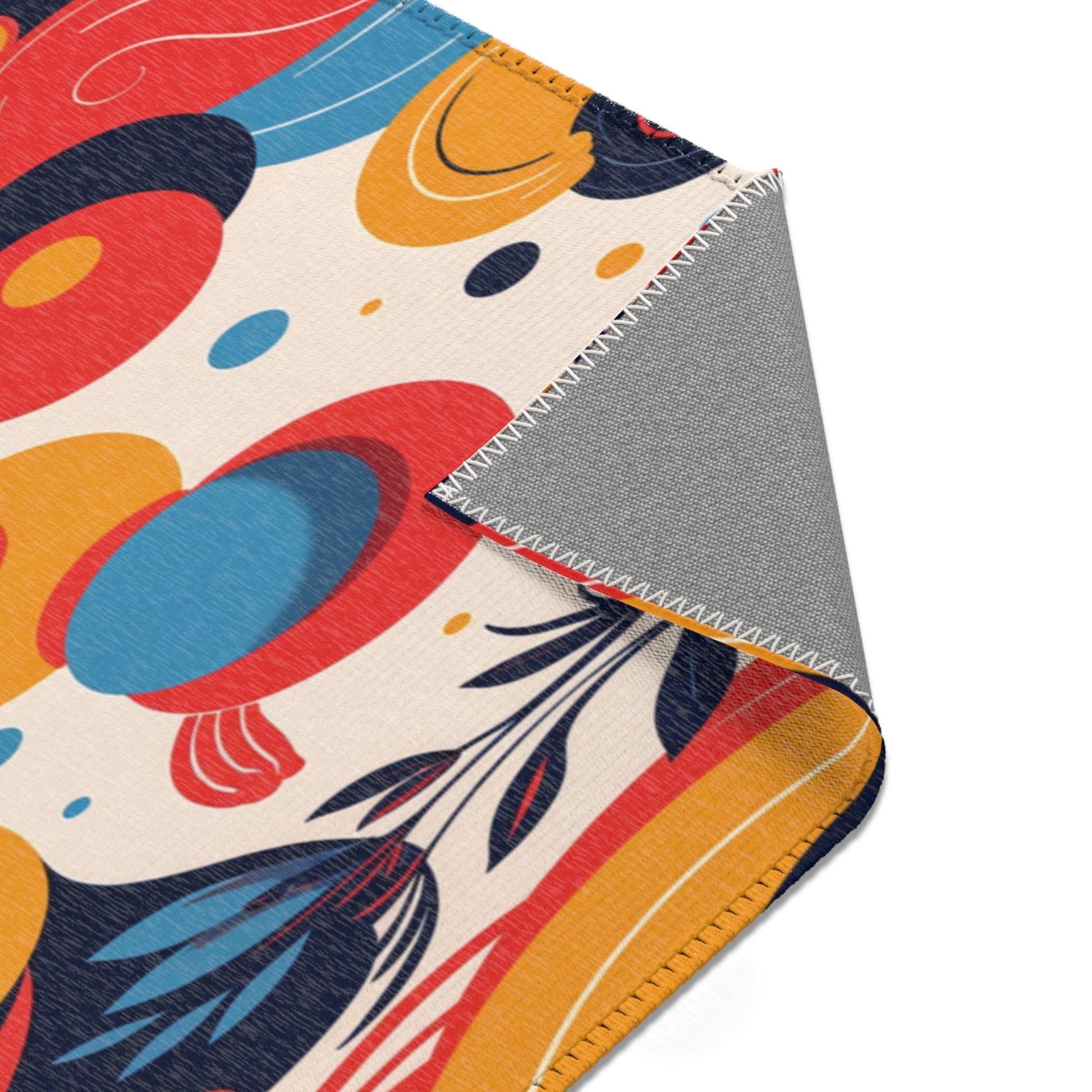 A close-up of a blanket with a colorful abstract pattern in red, blue, yellow, and black on a cream background. The corner is folded to reveal the solid gray underside, white zigzag stitching, and durable polyester chenille for stylish home decor.